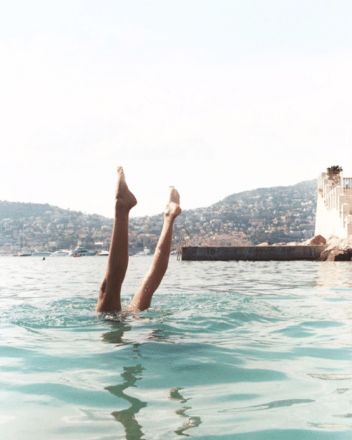 woman diving into ocean with legs sticking out of water