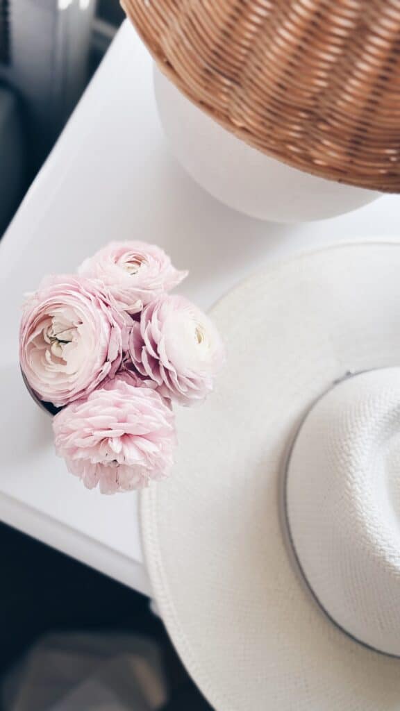 ranunculus bouquet next to white hat and rattan lamp