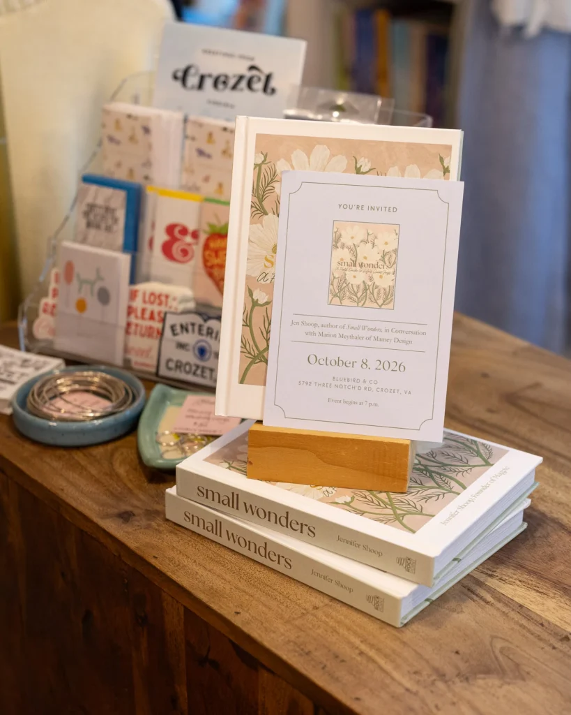 Copies of Small Wonders beneath an event invitation at Bluebird & Co in Crozet.
